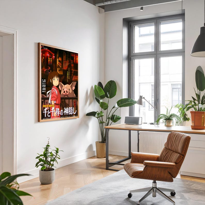 May include: A framed poster featuring artwork from the animated film "Spirited Away." The poster shows a young girl in a red outfit with a pig-like creature. Japanese text is visible at the bottom. The poster is displayed on a white wall.