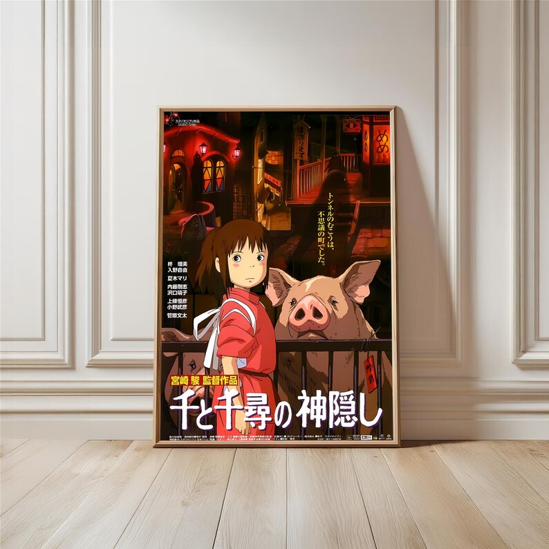 May include: Framed poster featuring a scene from the animated film "Spirited Away." The artwork depicts a young girl in a red outfit, standing near a pig. The background shows a nighttime cityscape with Japanese text. The poster is in a wooden frame.