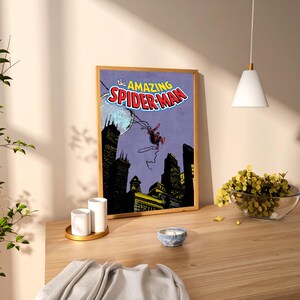 May include: A framed print of The Amazing Spider-Man comic book cover. The artwork features Spider-Man swinging through a city skyline with a purple background. The title is in red and blue.