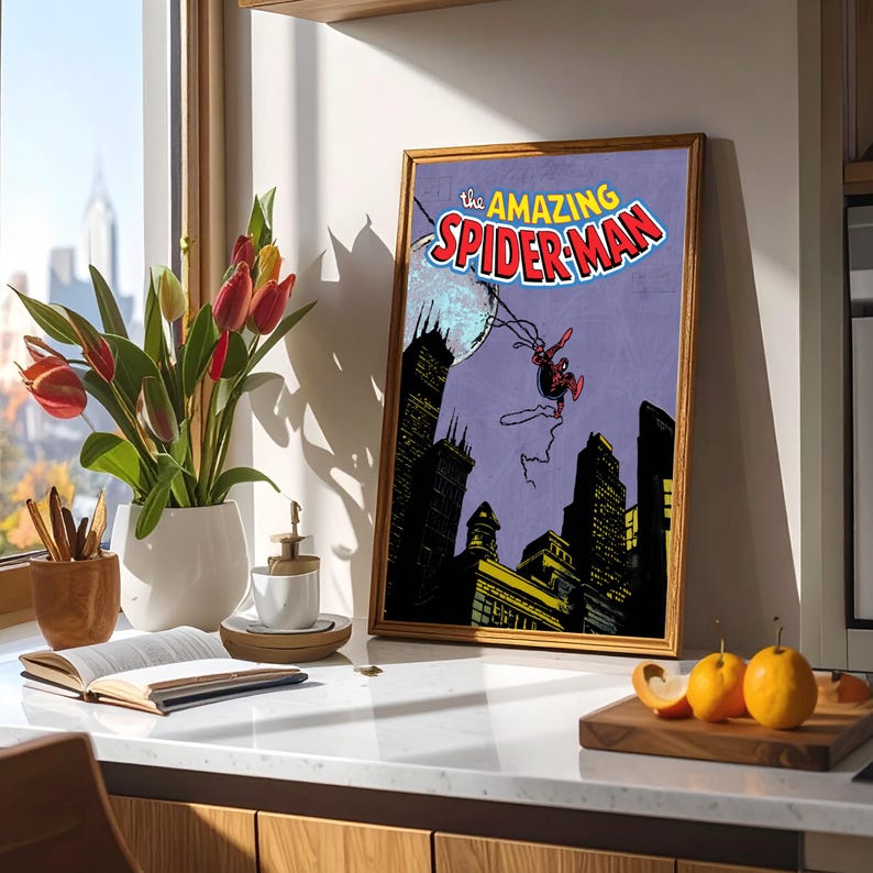 May include: A framed print of The Amazing Spider-Man comic book cover. The artwork features Spider-Man swinging over a city skyline with a purple background. The frame is a warm, light brown color.