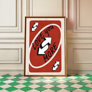 Può includere: Stampa artistica incorniciata con un design di carta rossa, con le parole "Love You More" e frecce inverse. L'opera d'arte è in una cornice dorata, su una parete bianca e un pavimento a scacchi verdi e bianchi.
