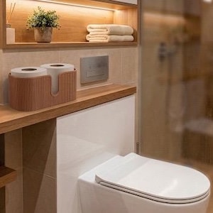 May include: A brown, ribbed, oval-shaped toilet paper holder containing two rolls of white toilet paper. The holder features a U-shaped cutout on the front and is positioned on a wooden bathroom counter next to a white toilet and a glass shower.