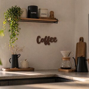 May include: A kitchen scene with coffee-making equipment and decor. A black kettle, glass pour-over, and wooden cutting board sit on the counter. A wooden shelf holds coffee and sugar canisters. A wooden sign spells "Coffee".