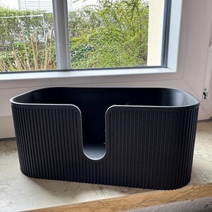 May include: A black, oval-shaped storage container featuring a vertical ribbed texture on the exterior walls. The front side of the container has a deep, U-shaped cutout that extends from the top rim toward the base, creating an open access point.