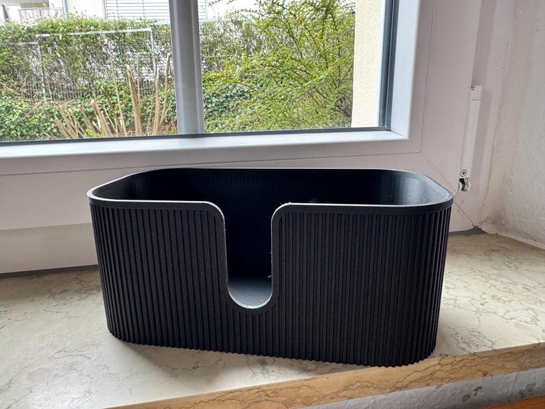 May include: A black, oval-shaped storage container featuring a vertical ribbed texture on the exterior walls. The front side of the container has a deep, U-shaped cutout that extends from the top rim toward the base, creating an open access point.