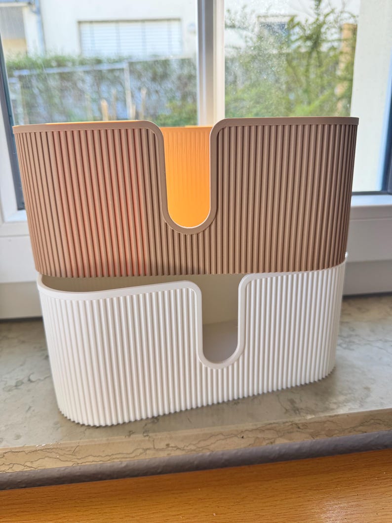 May include: A two-tiered storage organizer featuring a ribbed texture on the exterior. The top section is a tan color, while the bottom section is white. Both tiers have a U-shaped cutout on the front panel, allowing for easy access to items stored inside.