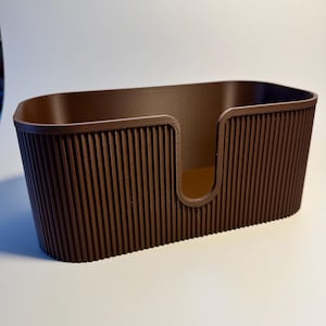 May include: A dark brown, oval-shaped storage container featuring a vertical ribbed texture on the exterior walls. The front side of the container includes a U-shaped cutout that extends from the top rim toward the base, creating an open access point.