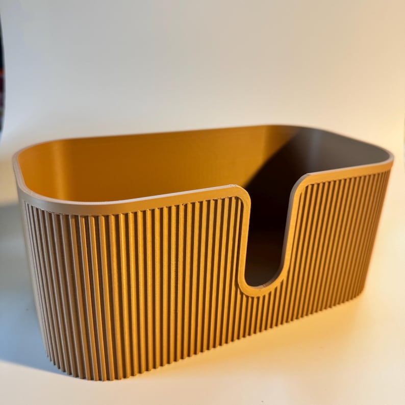 May include: An oval-shaped storage bin in a solid mustard yellow color. The exterior features a vertical ribbed texture throughout the sides. The front side includes a U-shaped cutout opening that extends from the top rim toward the base.