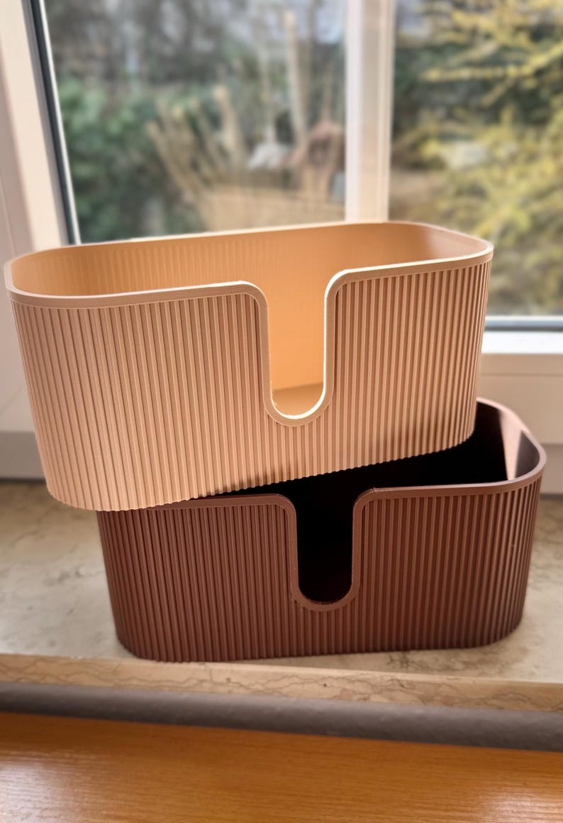 May include: Two oval-shaped storage bins with a vertical ribbed texture on the exterior. The top bin is light beige, and the bottom bin is dark brown. Each bin features a U-shaped cutout on the front side, allowing for easy access to contents.