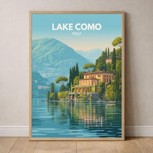 Può includere: Una stampa artistica incorniciata del Lago di Como, Italia. L'illustrazione raffigura una serena scena lacustre con una villa su una collina, circondata da una vegetazione lussureggiante e montagne. Il cielo è blu e l'acqua riflette il paesaggio.