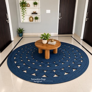 May include: A large, round, dark blue braided rug featuring a concentric pattern of smaller circular woven accents. The rug is centered on a light-colored floor and displays the text Sanwaliya Rugs in white lettering near the bottom edge.