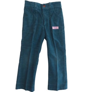 May include: Teal corduroy pants with a button closure and front pockets. A small pink label is sewn on the right pocket. The pants have a flared leg design.