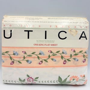 May include: A packaged king flat sheet by Utica. The sheet features a floral design with blue and pink flowers and green leaves on a white background. The packaging includes text that reads "Utica" and "One King Flat Sheet".