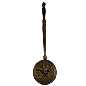 May include: Antique bronze waffle iron with a long wooden handle. The round iron features a detailed relief scene of figures around a table. The handle is approx. 46 cm long.