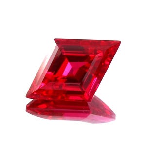 May include: A faceted, kite-shaped gemstone in a vibrant red hue. The gem has a symmetrical design with multiple facets that reflect light, creating a brilliant sparkle. The gemstone is displayed on a reflective surface, enhancing its visual appeal.