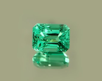Könnte beinhalten: Ein lebendiger, smaragdgeschliffener Edelstein mit leuchtend grüner Farbe. Der rechteckige Edelstein weist präzise geschliffene Facetten auf, die das Licht reflektieren und einen funkelnden Effekt erzeugen. Der Edelstein wird auf einer reflektierenden Oberfläche präsentiert.