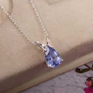 Könnte beinhalten: Eine silberne Halskette mit einem birnenförmigen, facettierten hellvioletten Edelsteinanhänger in einer Vier-Krappen-Fassung. Die zarte Silberkette ist über eine einfache, polierte Metallöse mit dem Anhänger verbunden.