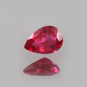 以下が含まれることがあります： 鮮やかな赤色の、梨型のファセットルビーの宝石。 宝石は反射とともに表示され、そのカットと輝きを示しています。 この宝石は愛と情熱の象徴です。