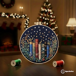 Puede incluir: Un bastidor redondo con tela azul marino bordada con libros, flores y estrellas. Bobinas de hilo verde y rojo están delante. Un árbol de Navidad y una chimenea son visibles en el fondo.