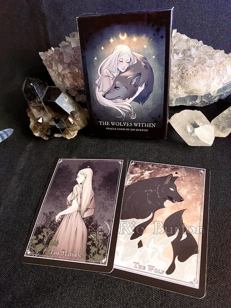 May include: A box of oracle cards titled "The Wolves Within" by Rio Burton. The box features a woman with long white hair holding a wolf. The cards are illustrated with a woman and a wolf.