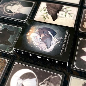 May include: A deck of oracle cards called "The Wolves Within" with a black background and silver lettering. The box features an illustration of a woman with long white hair holding a wolf in her arms. The cards are designed for self-discovery and spiritual guidance.