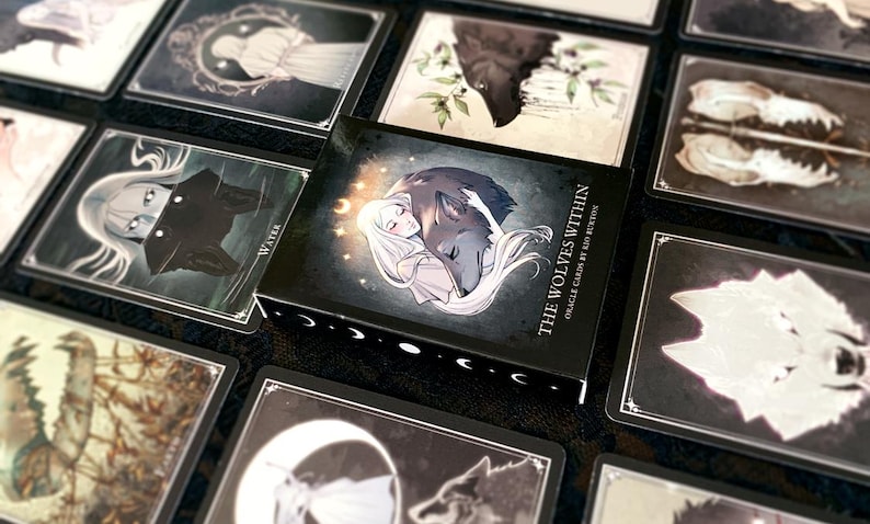 May include: A deck of oracle cards called "The Wolves Within" with a black background and silver lettering. The box features an illustration of a woman with long white hair holding a wolf in her arms. The cards are designed for self-discovery and spiritual guidance.
