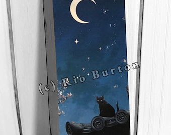 May include: A bookmark featuring a night sky scene with a crescent moon and stars. A black cat sits atop a dark structure. The text "(c) Rio Burton" is printed on the bookmark.
