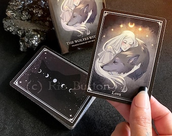May include: A black and white oracle card with a woman holding a wolf. The card has a crescent moon and stars in the background. The text on the card reads "THE WOLVES WIT ORACLE CARDS BY RIO BUK" and "LOVE".