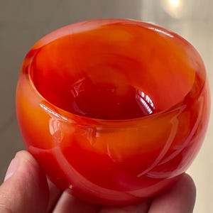 May include: A hand-blown glass bowl with a vibrant orange and red colour gradient. The bowl has a rounded shape with a wide opening, showcasing the glossy, reflective surface of the glass. This decorative bowl is suitable for home decor.