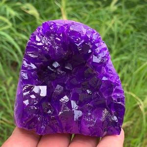Könnte beinhalten: Eine leuchtend tiefviolette Kristallgruppe mit einer gezackten, facettierten Oberfläche. Das Mineralexemplar weist zahlreiche scharfe, kantige Spitzen auf, die das Licht einfangen und ein brillantes, durchscheinendes Erscheinungsbild erzeugen.