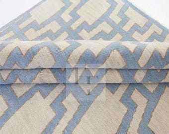 May include: A folded rug with a geometric pattern in light blue and off-white. The rug's design features a repeating series of angular shapes, creating a modern and stylish look. The rug is made of a woven material, and the folded section reveals the texture and thickness.