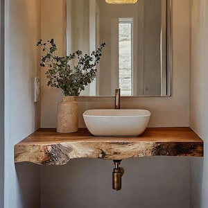 Puede incluir: Un tocador de baño moderno con una encimera de madera de borde vivo. Un lavabo rectangular blanco se asienta sobre la madera, con un grifo de latón. Un jarrón con vegetación y un espejo completan el diseño.