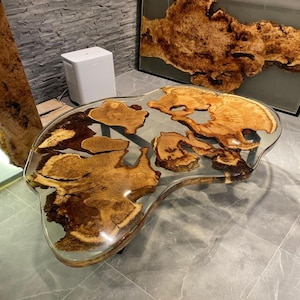 Puede incluir: Una mesa de centro única con una tapa de resina transparente, que muestra patrones naturales de vetas de madera. El diseño de la mesa incorpora formas orgánicas y mide aproximadamente 122 cm de largo y 61 cm de ancho.