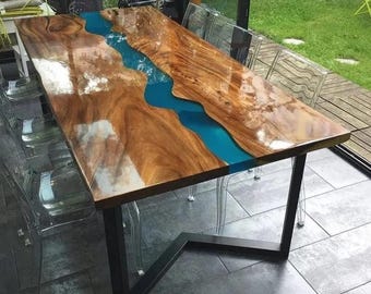 Puede incluir: Una mesa rectangular de madera con acabado brillante. La mesa presenta un río de resina azul en el centro, creando un diseño único. Se apoya en patas de metal negro.