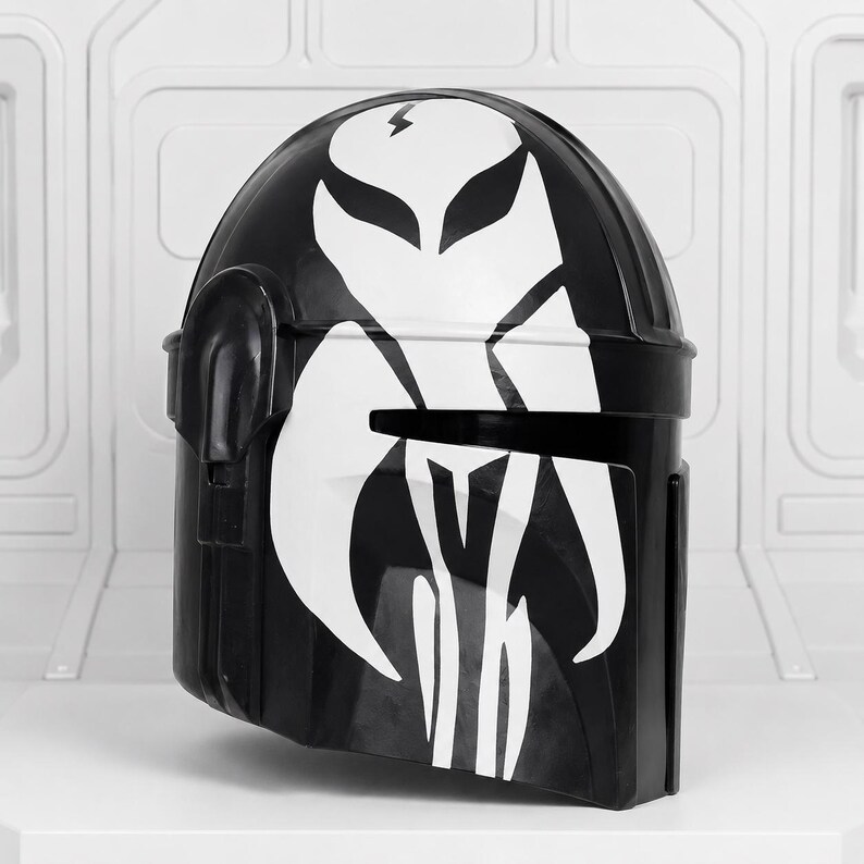 May include: Black helmet with a white graphic design. The helmet features a stylized white emblem on the front and top, with a lightning bolt symbol. The helmet is likely a costume piece or collectible.