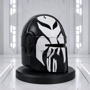 May include: A black helmet with a white graphic design, displayed on a black stand. The helmet's design features a stylized skull-like pattern across the front and top, with a glossy finish. The background is a white, futuristic-looking room.