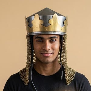 May include: A metal crown helmet featuring a pointed steel top and a brass band with decorative fleur-de-lis cutouts. Attached to the base is a gold-toned chainmail aventail that hangs down to cover the sides of the head and neck area.