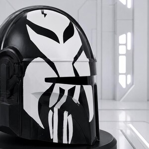 May include: A black helmet with a white graphic design. The helmet has a glossy finish and a distinctive, stylized face design in white. The design includes a lightning bolt and angular shapes. The helmet is likely for cosplay or display.