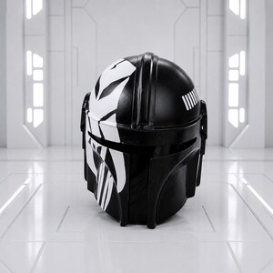 May include: A black and white Mandalorian helmet with a distinctive design. The helmet features a glossy black finish with white graphic accents on the top and face. The design includes vertical stripes and a series of parallel lines on the back.