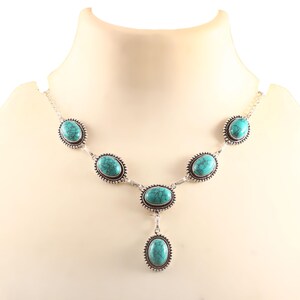 May include: A silver necklace with oval turquoise gemstones. The necklace features a series of turquoise stones linked by silver, with a central pendant. The stones are a vibrant turquoise colour, set in a decorative silver frame.