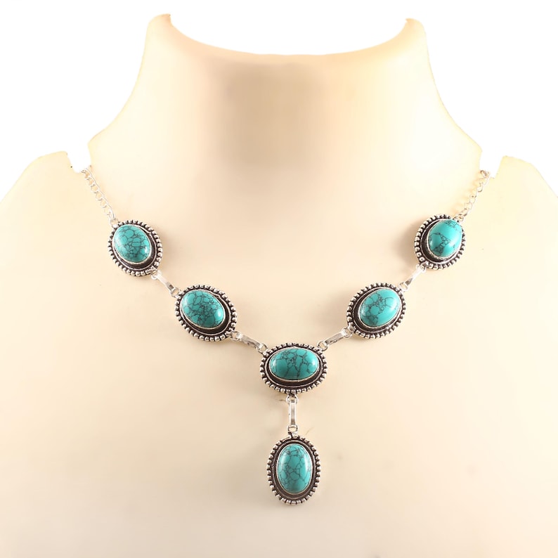 May include: A silver necklace with oval turquoise gemstones. The necklace features a series of turquoise stones linked by silver, with a central pendant. The stones are a vibrant turquoise colour, set in a decorative silver frame.