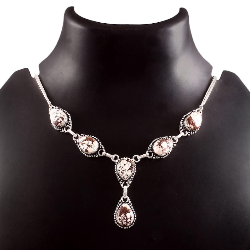 Puede incluir: Un collar plateado con piedras ovaladas y en forma de l&aacute;grima. Las piedras tienen un patr&oacute;n moteado blanco y marr&oacute;n. El collar se exhibe en un maniqu&iacute; negro.
