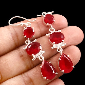 May include: Silver dangle earrings with vibrant red gemstones. Each earring features a series of round and teardrop-shaped stones, connected by silver links. The gemstones have a faceted cut, catching the light and creating a sparkling effect. The earrings are designed for pierced ears.