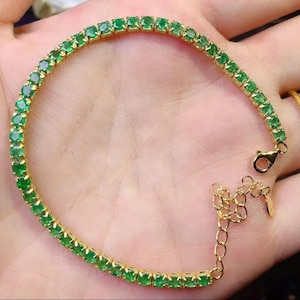 May include: A gold bracelet featuring a row of vibrant green gemstones. The bracelet has a delicate design with a secure clasp and adjustable chain. The gemstones are evenly spaced and add a touch of elegance.