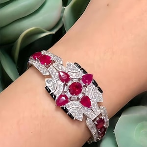 May include: A dazzling bracelet featuring a geometric design with vibrant red gemstones and sparkling white diamonds. The bracelet's intricate pattern includes black accents, creating a striking contrast. The bracelet is a luxurious piece of jewelry.