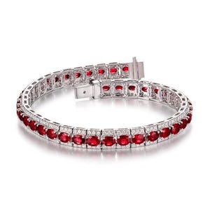 May include: A silver bracelet with oval-cut red gemstones and small, clear accent stones. The bracelet is open, showing the clasp and the intricate setting of the gemstones. The gemstones are evenly spaced along the bracelet's length.