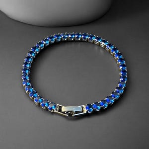 May include: A silver-toned bracelet with a row of vibrant blue gemstones. The bracelet is circular, with a secure clasp. The gemstones are a deep, rich blue color, creating a striking contrast against the silver metal.