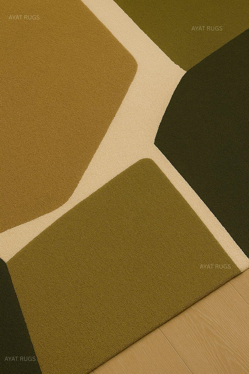 May include: A close-up of a modern area rug with an abstract design. The rug features geometric shapes in shades of olive green, brown, and cream. The rug is made of a soft, textured material and is suitable for living rooms and bedrooms.
