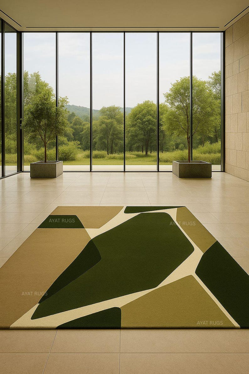 May include: A modern area rug with an abstract geometric design in shades of green, beige, and cream. The rug is rectangular and features the text "AYAT RUGS" in several places. The rug is placed on a tiled floor in front of a large window.