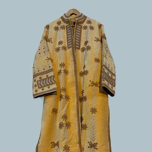Pode incluir: Um casaco longo amarelo com bordados florais e acabamentos marrons. O casaco apresenta gola mandarim e mangas compridas com bordados detalhados nos punhos. O padr&atilde;o floral &eacute; repetido em toda a pe&ccedil;a.